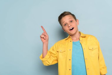 Şok olmuş ve sevimli çocuk mavi arka planı işaret ediyor. 