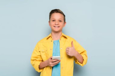 Akıllı telefonu tutan gülümseyen çocuk mavi arka planda gibi görünüyor. 
