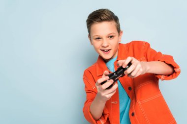 KYIV, UKRAINE - 21 HAZİRAN 2020: Mavi arka planda joystick ile oynayan gülümseyen çocuk 