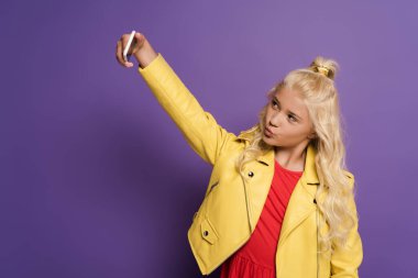 Tatlı çocuk selfie çekiyor ve mor arka planda hava öpücüğü gösteriyor. 