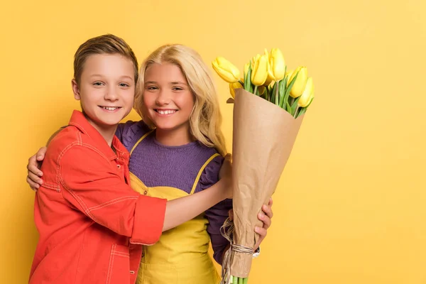 Menino Sorridente Abraçando Amigo Com Buquê Fundo Amarelo — Fotografia de Stock