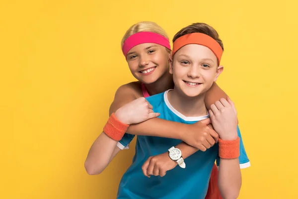 Uśmiechnięte Dzieci Odzieży Sportowej Przytulające Się Patrzące Kamerę Żółtym Tle — Zdjęcie stockowe
