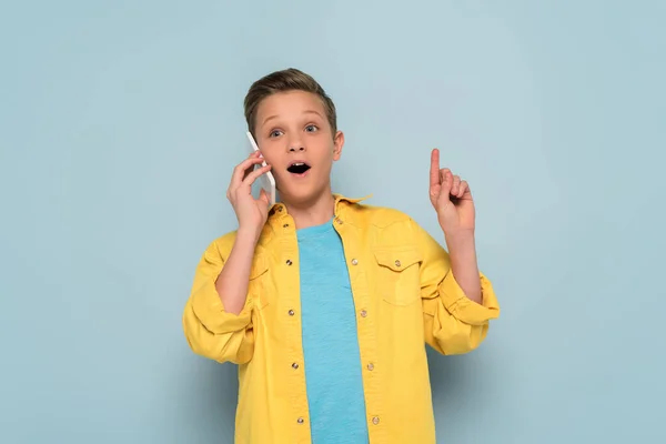 Überraschtes Kind Spricht Auf Smartphone Und Zeigt Ideengeste Auf Blauem — Stockfoto