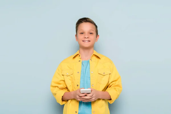 Niño Sonriente Sosteniendo Teléfono Inteligente Mirando Cámara Fondo Azul — Foto de Stock