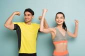 šťastný atletický pár stojící ve sportovním oblečení ukazuje svaly na modré