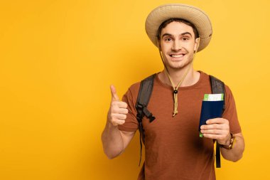 Sırt çantalı neşeli turist elinde pasaport ve biletle sarıda boy gösteriyor.