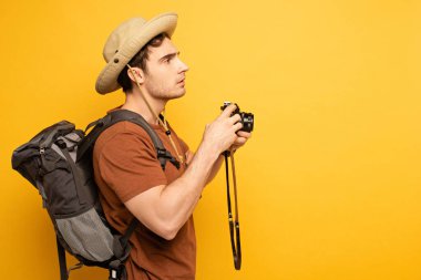Sırt çantalı yakışıklı gezgin sarıda fotoğraf makinesi tutuyor.