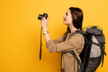 Sırt çantalı heyecanlı turist sarıda fotoğraf makinesi tutuyor.
