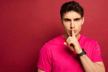 Kırmızı üzerinde sessizlik sembolü olan pembe tişörtlü bir adamın portresi.