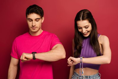 happy couple looking at wristwatches on red clipart