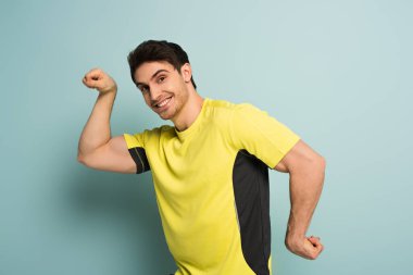 Kaslı, gülümseyen, mavi tişörtlü sporcu.