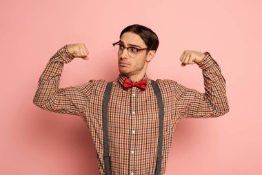 thoughtful male nerd in eyeglasses showing muscles on pink clipart