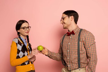 couple of smiling nerds in eyeglasses holding apple on pink clipart