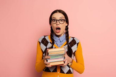 shocked female nerd with open mouth holding books on pink clipart