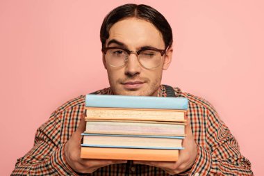 winking male nerd in eyeglasses holding books, Isolated on pink clipart