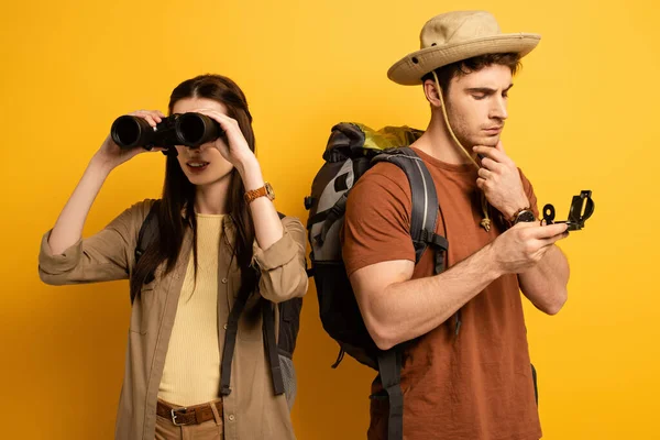 一对带着背包和双筒望远镜的游客看着黄色的指南针 — 图库照片