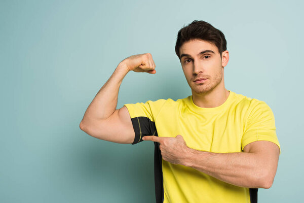 muscular sportsman in yellow t-shirt pointing at muscles on blue