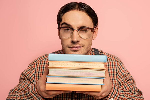 winking male nerd in eyeglasses holding books, Isolated on pink