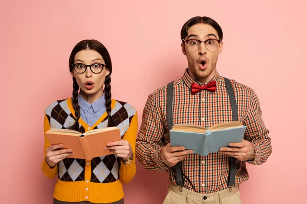 couple of shocked nerds in eyeglasses reading books on pink