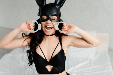 Erotik tavşan maskeli, yatakta kelepçe ısıran seksi bir kadın.