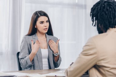 Selective focus of employee pointing oneself and talking to african american recruiter at job interview in office clipart