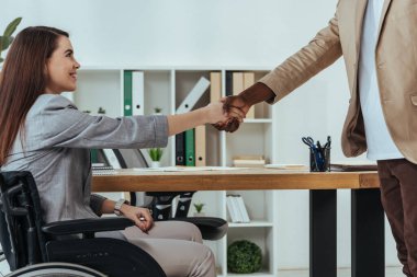 Disabled employee and african american recruiter shaking hands at job interview in office clipart
