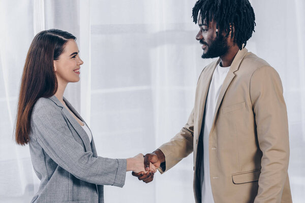 African american employee and recruiter looking at each other, smiling and shaking hands in office