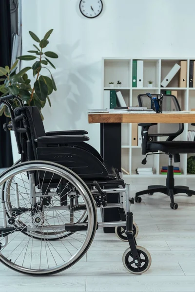 テーブルの近くの黒い車椅子とオフィスの植物 — ストック写真