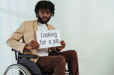 Disabled african american man with placard with looking for a job lettering on wheelchair on white  clipart