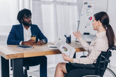 African american recruiter and disabled employee on wheelchair talking at table in office clipart