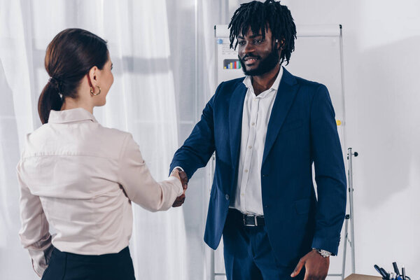 Африканский американский рекрутер и сотрудник пожимают друг другу руки, улыбаются и смотрят друг на друга
