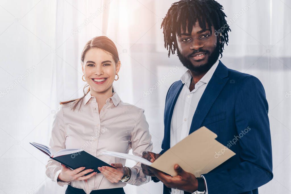 African american employer with folder and recruiter with notebook smiling and looking at camera  