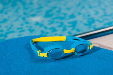 swim goggles on flutter board in swimming pool  clipart
