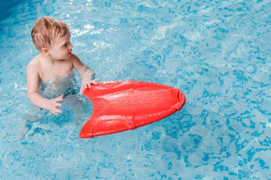 Yüzme havuzunda kanat çırpan tahtayla yüzen tatlı çocuk. 
