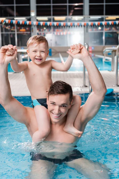 快乐的游泳教练把可爱的幼儿抱在游泳池的肩上 — 图库照片