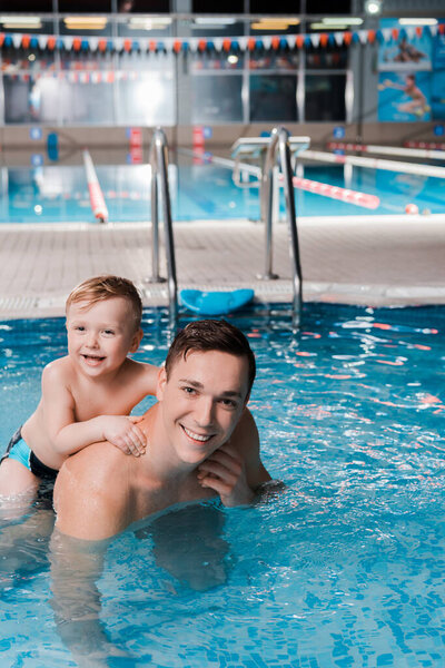 happy toddler kid and swim coach looking at camera in swimming pool 