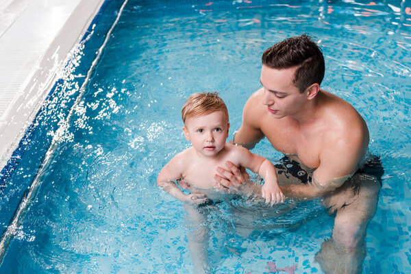swim instructor teaching cute toddler boy in swimming pool 