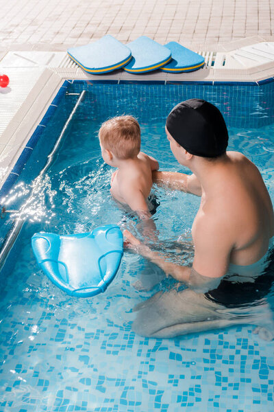 swim coach in swimming cap swimming with toddler kid in swimming pool 