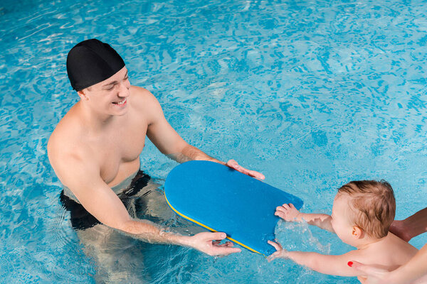 overhead view of mother touching cute toddler boy swimming near swim instructor 