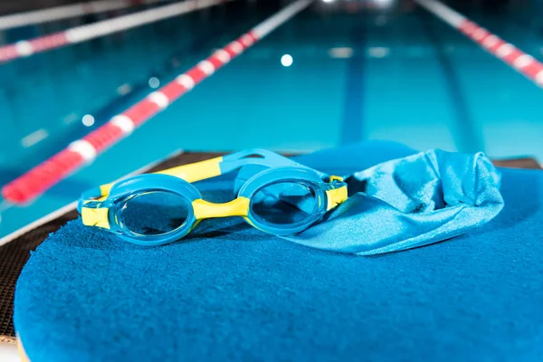 goggles and swimming cap on flutter board near swimming pool with blue water