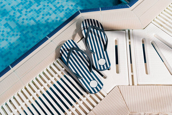 top view of flip flops near swimming pool with blue water 