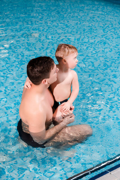 swim coach holding in arms cute toddler boy in swimming pool 