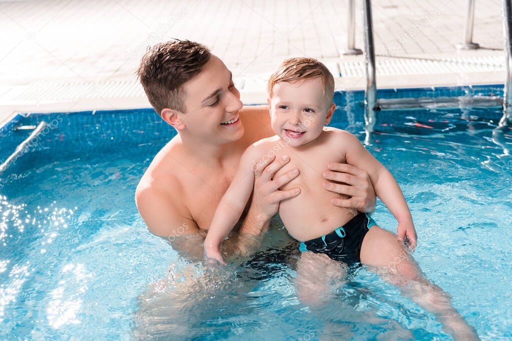 happy swim trainer swimming with toddler boy in swimming pool 
