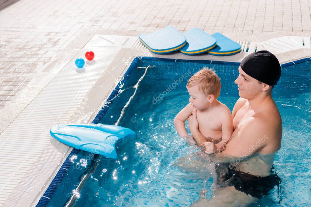 side view of cheerful swim coach swimming with toddler kid in swimming pool 
