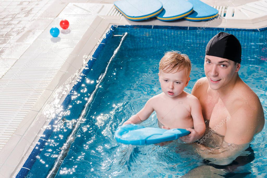 happy swim coach in swimming cap teaching toddler kid in swimming pool 