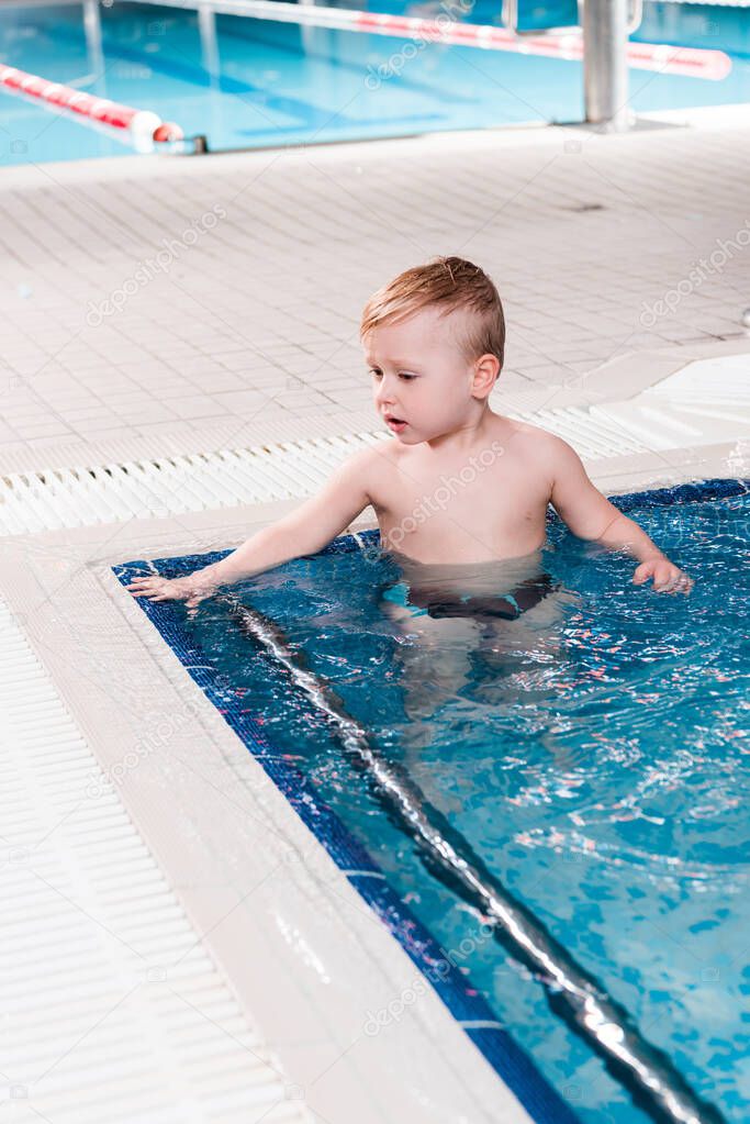 cute toddler boy in swimming pool with blue water 