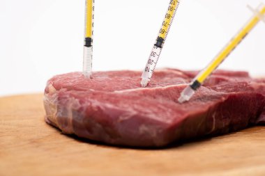 Selective focus of syringes in raw meat on cutting board isolated on white clipart
