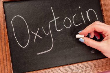 Cropped view of woman holding piece of chalk near blackboard with oxytocin lettering clipart