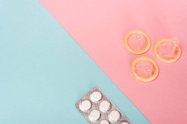 Pembe ve mavi yüzeyde doğum kontrol hapları ve prezervatifleri olan su toplamasının en üst görüntüsü.