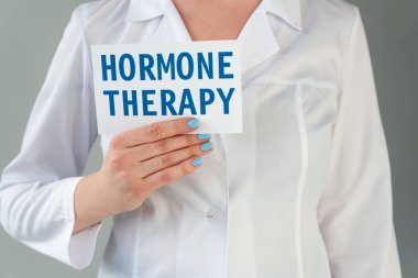 Cropped view of doctor in white coat holding card with hormone therapy lettering isolated on grey clipart